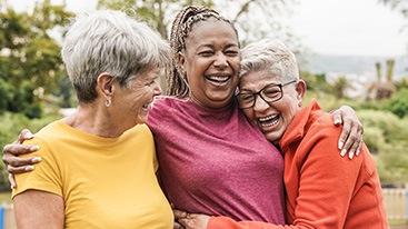 Three women in bright t-shirts outside laughing and hugging