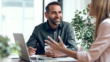 Two people chatting at table with computer and coffee