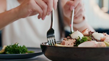 Hands scooping salad onto their plate with forks