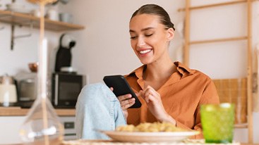 Woman smiling while looking at phone at home