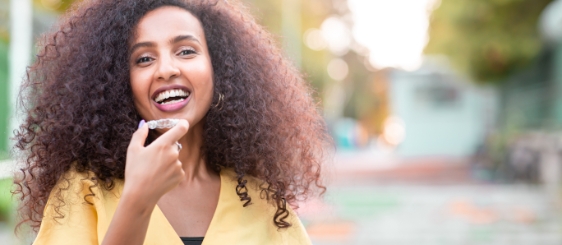 Smiling woman holding Invisalign clear aligner