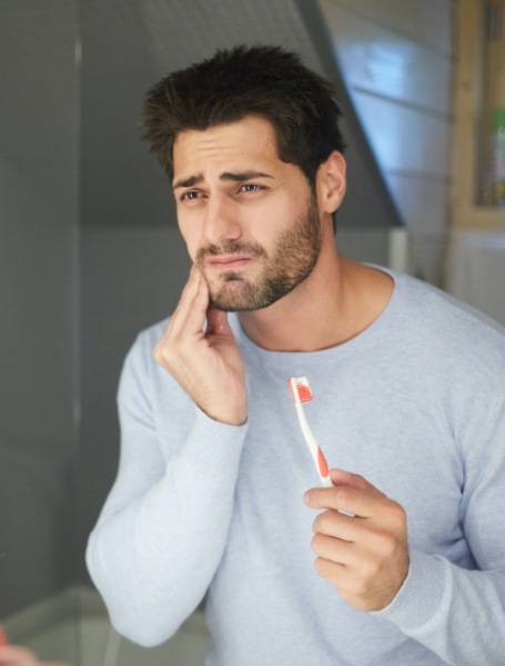 Man in need of emergency dentistry holding cheek in pain