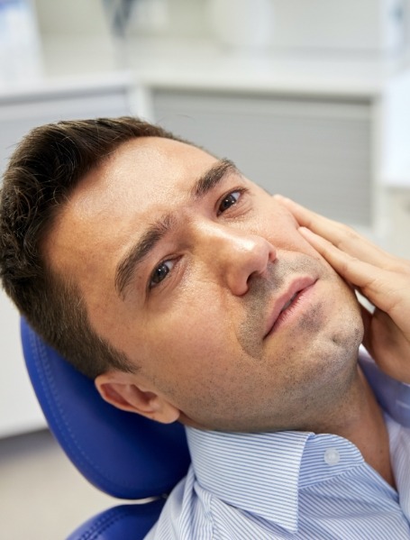 Man in need of emergency dentistry holding cheek in pain