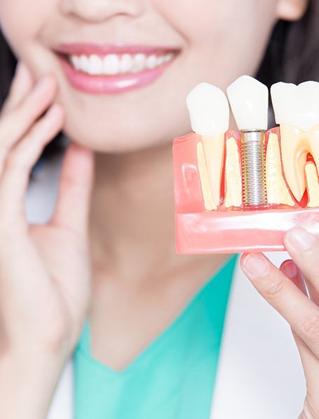 Dentist touching jaw with one hand and holding sample implant with the other
