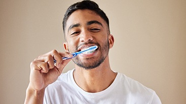 Man in white t-shirt brushing teeth with beige background