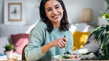 Woman in green sweater smiling as she forks a bite of her salad