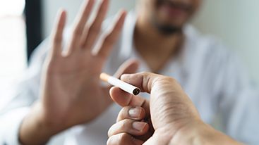 Man blurry in background holding out hand to refuse an offered cigarette