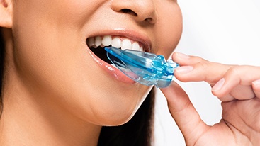 Nose-to-neck view of woman placing blue nightguard into her mouth