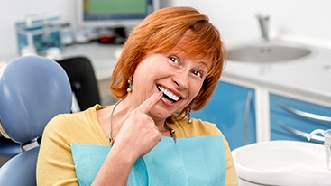 Woman with red hair in dental chair pointing to a tooth as she smiles