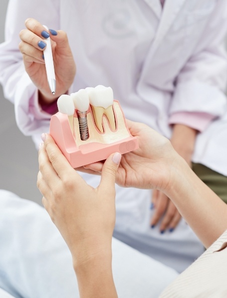 Dentist showing patient a model comparing dental implants to natural teeth