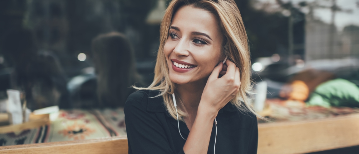 Woman smiling while placing white earbud in her ear