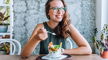 Woman with glasses smiling while eating breakfast