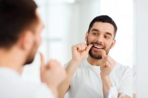 bearded man in white shirt flossing in front of mirror