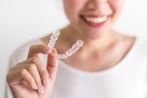 Woman wearing a white sweater and smiling while holding an Invisalign tray