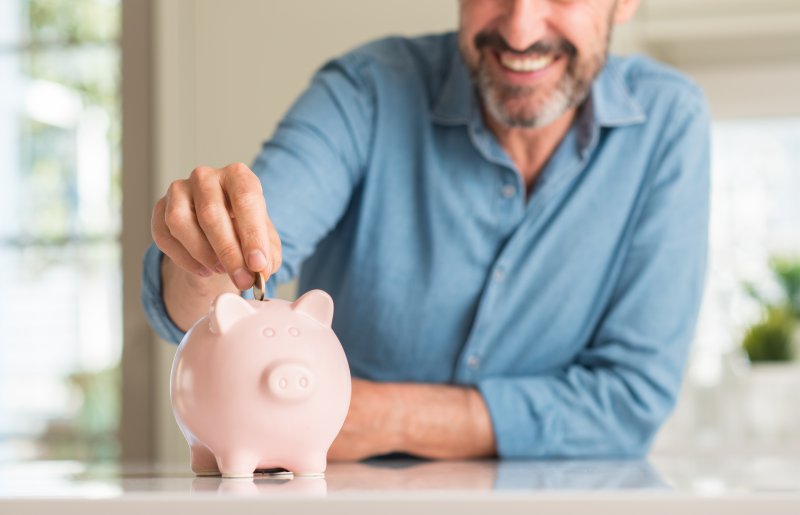Smiling middle-aged man saves money in piggy bank