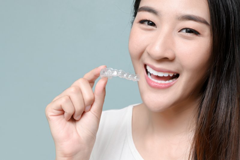 person holding Invisalign aligner tray and smiling