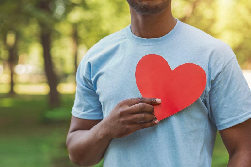 A hand holding a paper heart over a man’s chest.