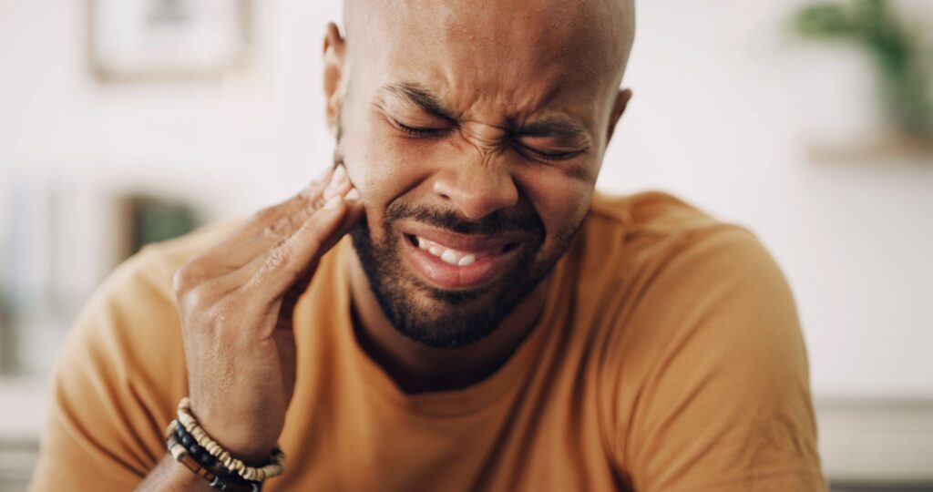 Man in yellow shirt touching jaw and squinting in pain