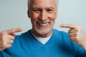 Senior man smiling and gesturing towards dentures.