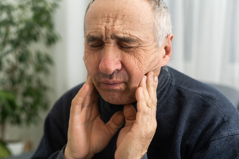 Older patient rubbing cheeks due to ill-fitting dentures